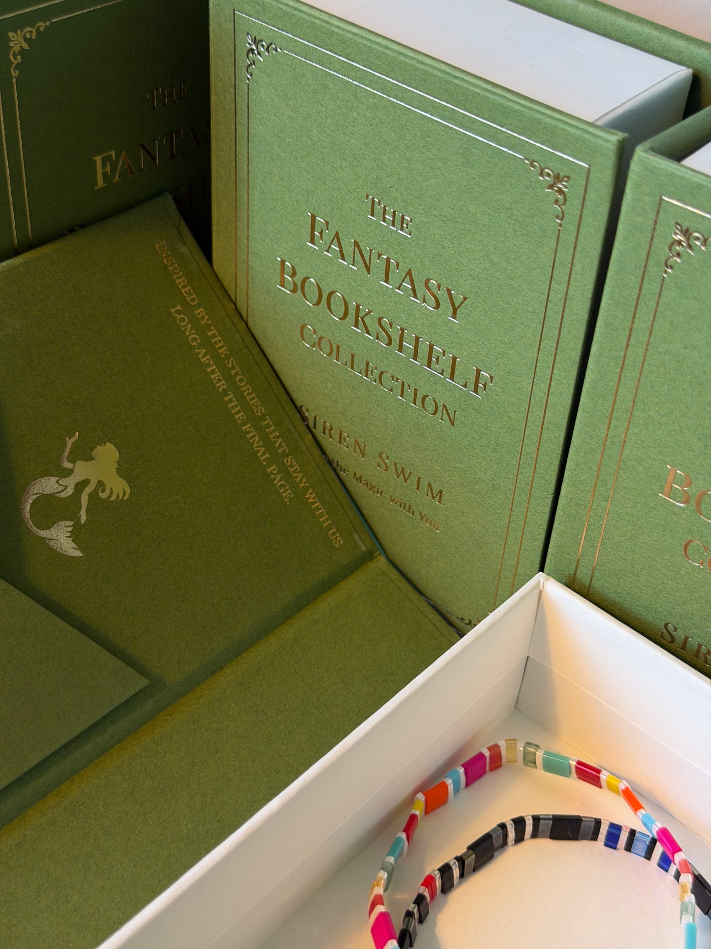 Fantasy Bookshelf Second Edition and Bat Brothers bracelets in an open green book-style Siren Swim jewelry box with gold lettering.