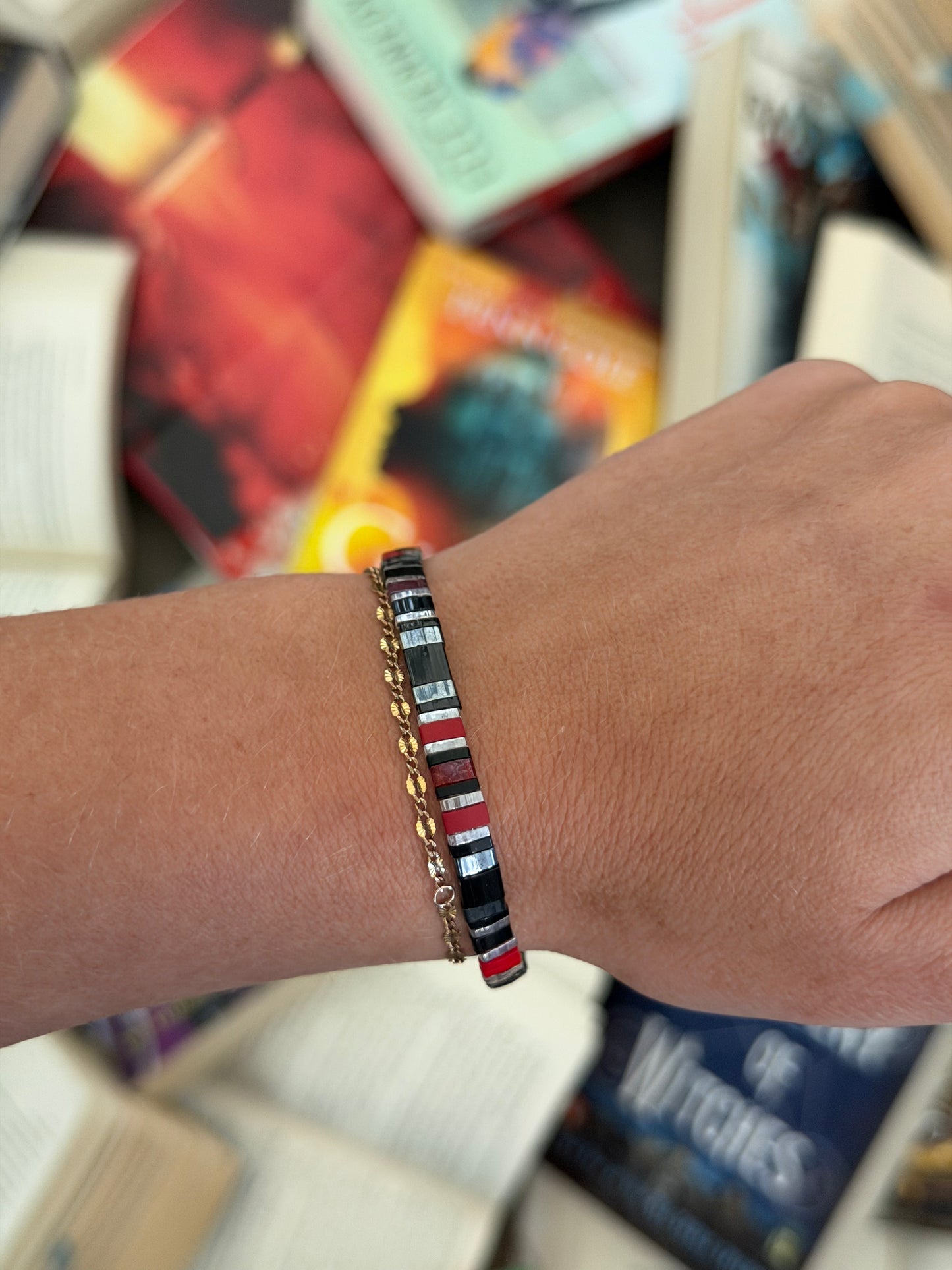 Bat Brothers bracelet showing deep red, black, and silver-toned glass beads on a wrist above scattered books.