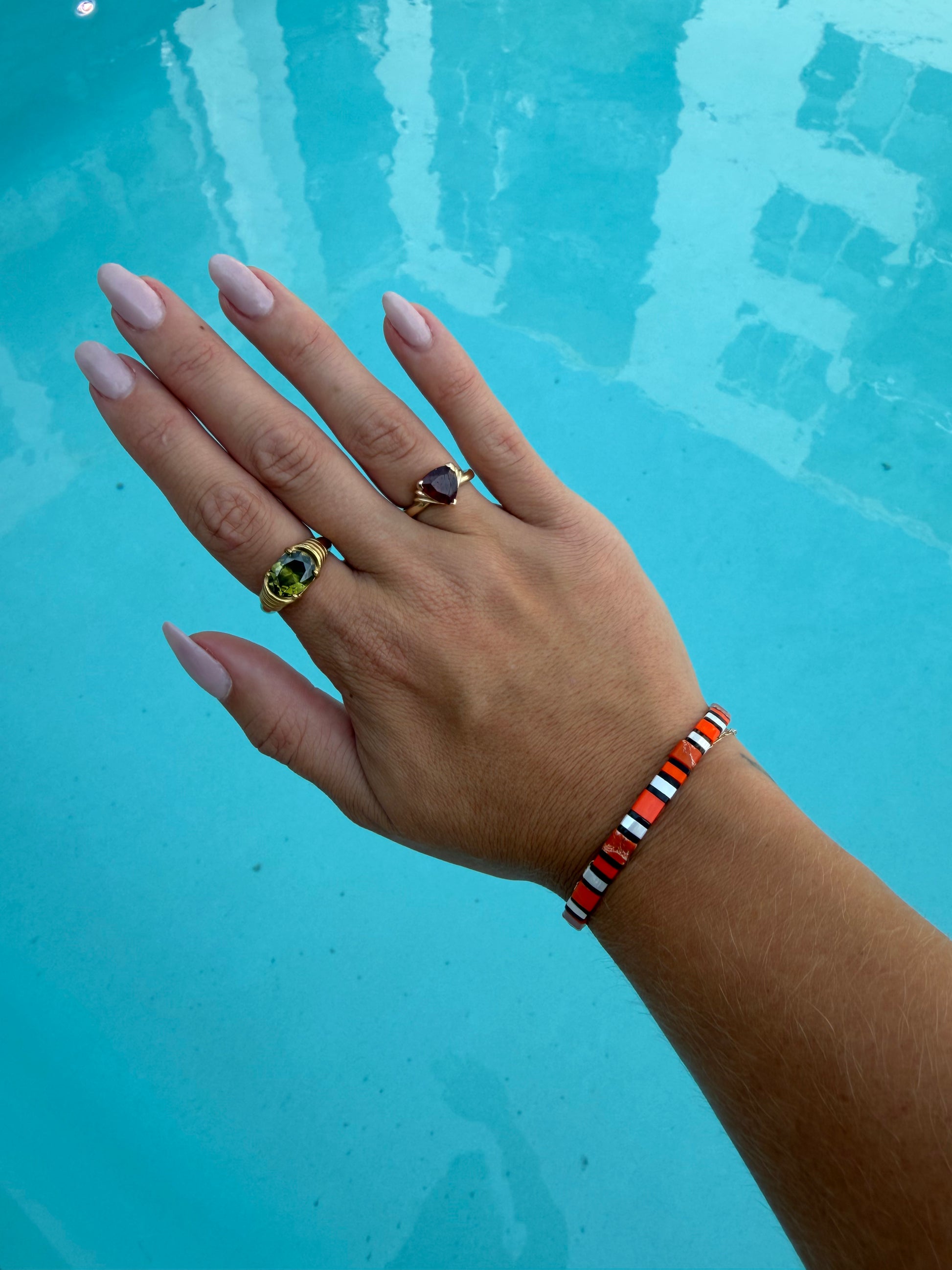 Clownfish-inspired orange, white, and black glass-bead bracelet worn on a wrist over bright blue pool water.