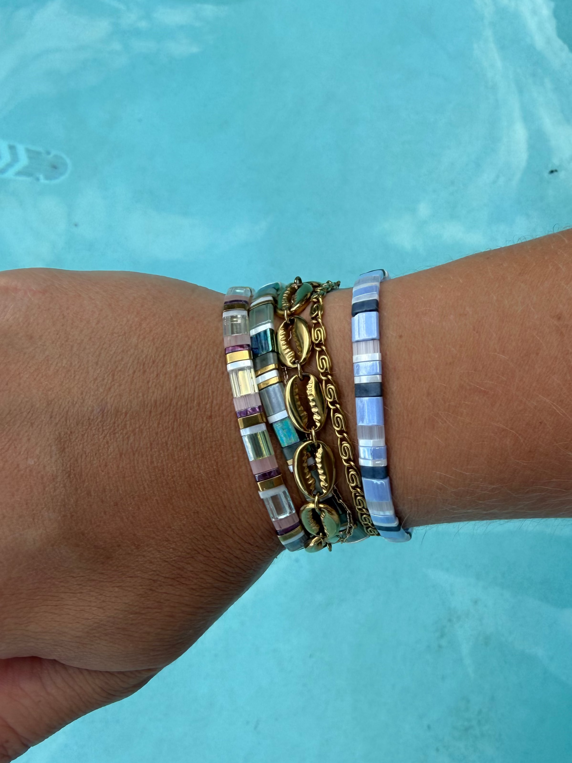 Island Cowrie and Whirlpool gold bracelets stacked between colorful glass bead bracelets by the pool.