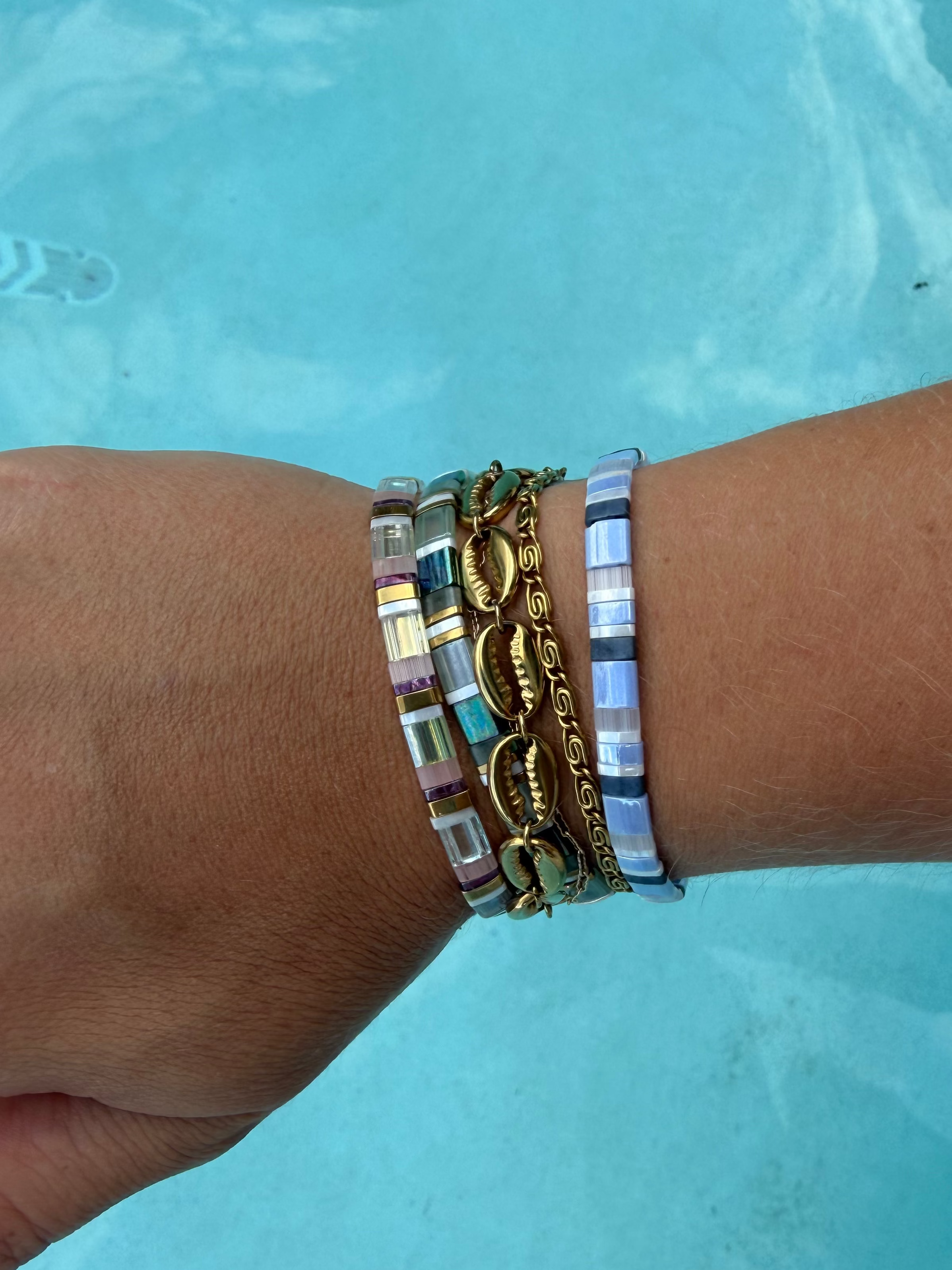 Island Cowrie and Whirlpool gold bracelets stacked between colorful glass bead bracelets by the pool.