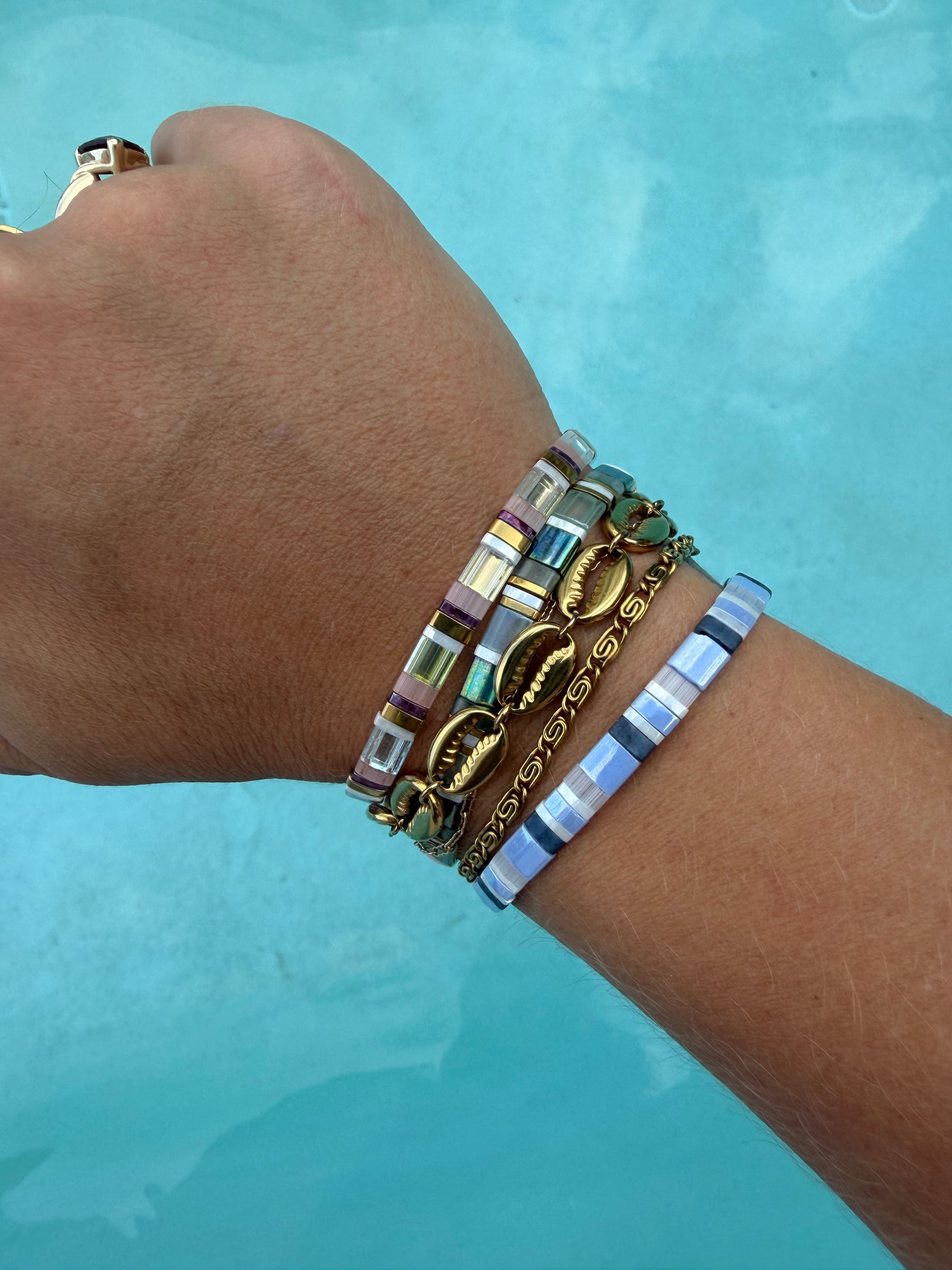 Gold Island Cowrie and Whirlpool bracelets layered with colorful Siren Swim glass bead bracelets.