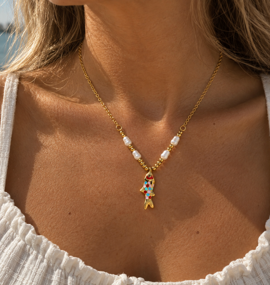 Rainbow Fish Necklace with colorful enamel fish charm, pearl details, and gold beads worn with a white top.
